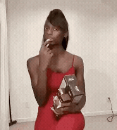 A Woman In A Red Dress Is Holding A Box Of Cereal And A Cigarette In Her Mouth . GIF