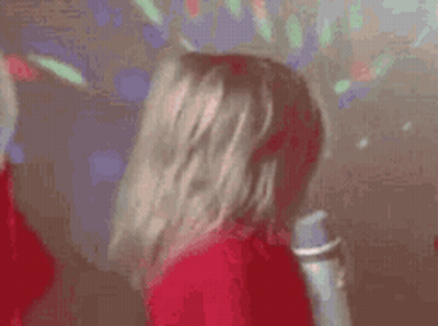 A Woman In A Red Dress Is Holding A Microphone And Dancing In A Disco Room . GIF