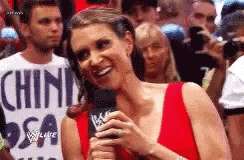 A Woman In A Red Dress Is Holding A Microphone And Smiling In Front Of A Crowd . GIF