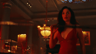 A Woman In A Red Dress Is Holding A Spear In A Dark Room GIF