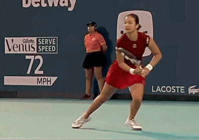 A Woman In A Red Dress Is Holding A Tennis Racquet In Front Of A Sign That Reads 72 Mph GIF