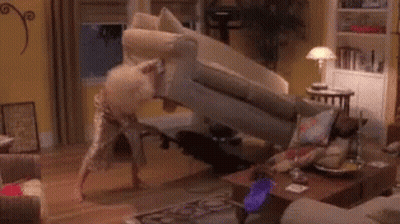 A Woman In A Red Dress Is Kneeling On A Couch In A Living Room With A Vacuum Cleaner . GIF