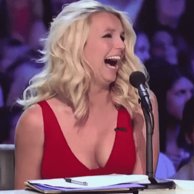 A Woman In A Red Dress Is Laughing While Sitting At A Microphone GIF