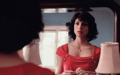 A Woman In A Red Dress Is Looking At Her Reflection In A Mirror GIF