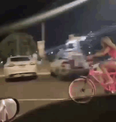 A Woman In A Red Dress Is Riding A Pink Bike Down The Street GIF