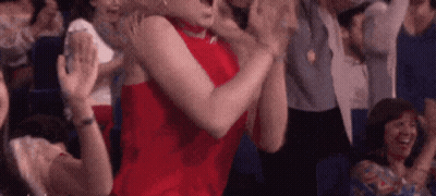 A Woman In A Red Dress Is Sitting In A Crowd Of People Clapping Their Hands . GIF