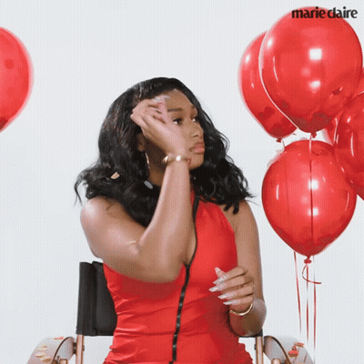 A Woman In A Red Dress Is Sitting In Front Of Red Balloons With Marie Claire Written On The Bottom Right GIF