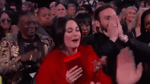 A Woman In A Red Dress Is Sitting In The Audience At A Concert . GIF