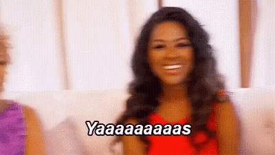 A Woman In A Red Dress Is Sitting On A Couch And Smiling While Saying Yaaa . GIF