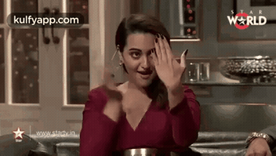 A Woman In A Red Dress Is Sitting On A Couch And Waving Her Hands . GIF