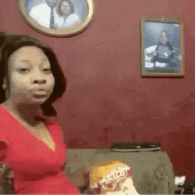 A Woman In A Red Dress Is Sitting On A Couch Holding A Bag Of Doritos Chips . GIF