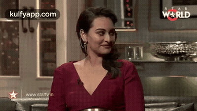 A Woman In A Red Dress Is Sitting On A Couch In A Living Room . GIF