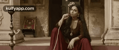 A Woman In A Red Dress Is Smoking A Hookah While Sitting On The Steps Of A Building . GIF