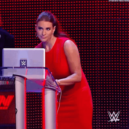 A Woman In A Red Dress Is Standing Behind A Podium With A Laptop On It . GIF