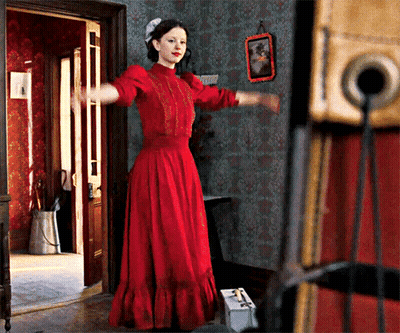 A Woman In A Red Dress Is Standing In A Doorway With Her Arms Outstretched GIF