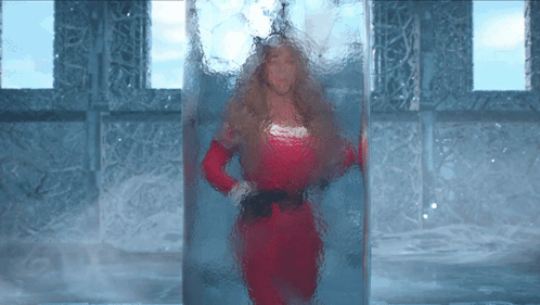 A Woman In A Red Dress Is Standing In A Glass Container GIF