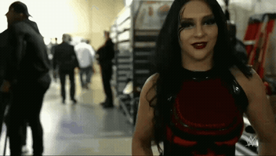 A Woman In A Red Dress Is Standing In A Hallway With People Walking Behind Her . GIF