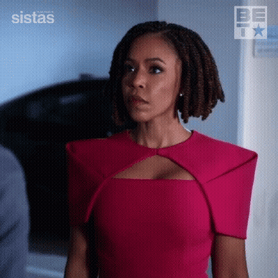 A Woman In A Red Dress Is Standing In A Room And Looking At The Camera . GIF