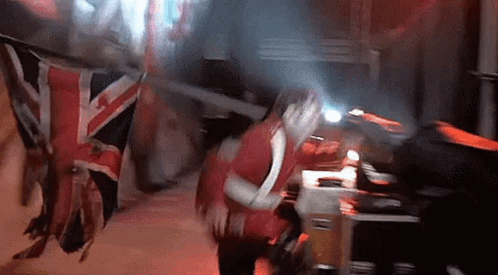 A Woman In A Red Dress Is Standing In Front Of A British Flag . GIF