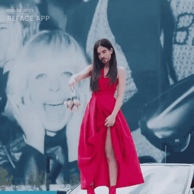 A Woman In A Red Dress Is Standing In Front Of A Car With A Reface App Logo On The Bottom GIF