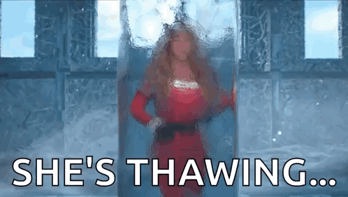 A Woman In A Red Dress Is Standing In Front Of A Glass Door With The Words `` She 'S Thawing ... '' GIF