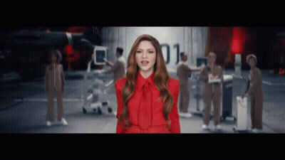 A Woman In A Red Dress Is Standing In Front Of A Group Of People With The Number 01 Behind Her GIF