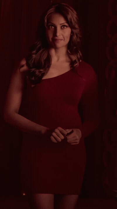 A Woman In A Red Dress Is Standing In Front Of A Red Wall GIF