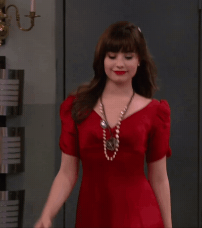 A Woman In A Red Dress Is Standing In Front Of A Wall GIF