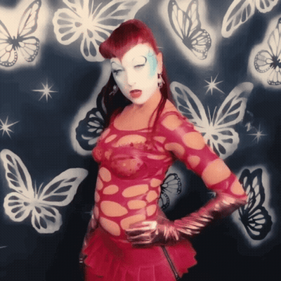 A Woman In A Red Dress Is Standing In Front Of A Wall With Butterflies On It GIF
