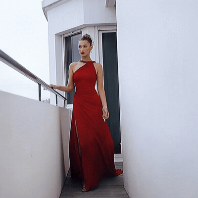 A Woman In A Red Dress Is Standing Next To A White Wall GIF