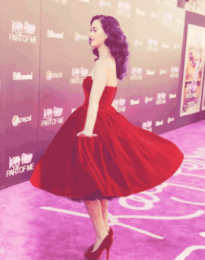 A Woman In A Red Dress Is Standing On A Purple Carpet With Pepsi And Billboard Signs Behind Her GIF