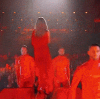A Woman In A Red Dress Is Standing On A Stage GIF