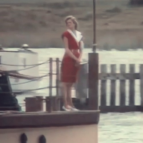 A Woman In A Red Dress Is Standing On The Side Of A Boat In The Water . GIF