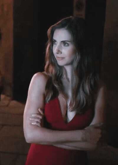 A Woman In A Red Dress Is Standing With Her Arms Crossed In Front Of A No Parking Sign GIF