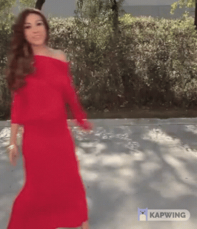 A Woman In A Red Dress Is Walking Down A Road . GIF