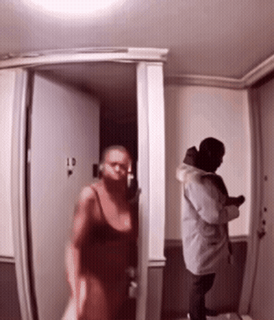 A Woman In A Red Dress Is Walking Into A Room With A Man In A Grey Coat GIF
