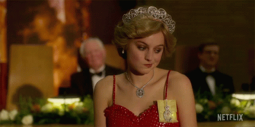 A Woman In A Red Dress Is Wearing A Tiara And Holding A Gold Medal .. GIF