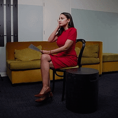 A Woman In A Red Dress Sits In A Chair GIF