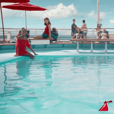 A Woman In A Red Dress Sits On The Edge Of A Large Swimming Pool GIF