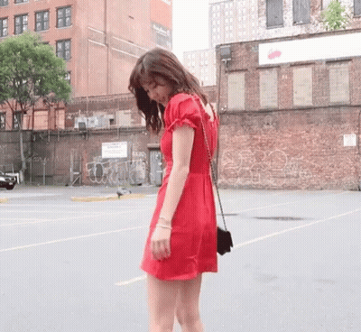 A Woman In A Red Dress Stands In Front Of A Brick Wall With Graffiti On It GIF