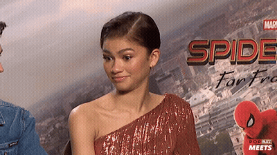 A Woman In A Red Dress Stands In Front Of A Poster That Says Spider-Man Far From Home GIF