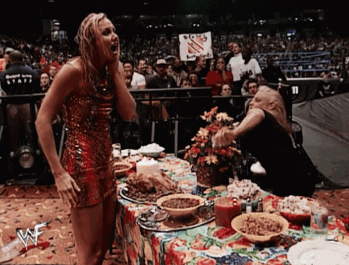 A Woman In A Red Dress Stands In Front Of A Table With A Wwe Logo GIF