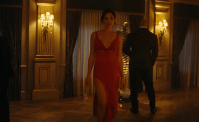 A Woman In A Red Dress With A Plunging Neckline Is Walking In A Room GIF