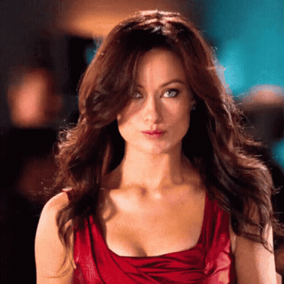 A Woman In A Red Dress With A Plunging Neckline Looks At The Camera GIF