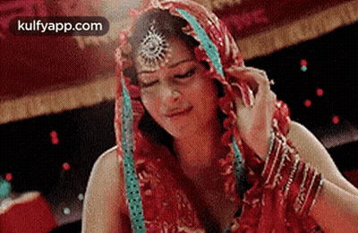 A Woman In A Red Dress With A Veil On Her Head Is Looking Down . GIF