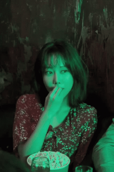 A Woman In A Red Floral Dress Is Eating Popcorn In A Dark Room GIF