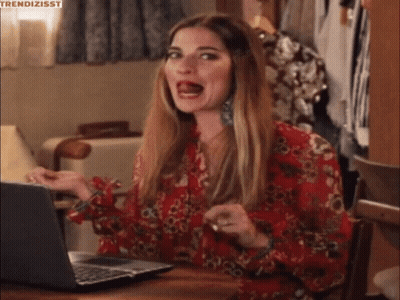 A Woman In A Red Floral Shirt Is Sitting At A Table With A Laptop . GIF