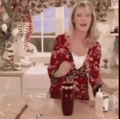 A Woman In A Red Floral Shirt Is Standing In A Kitchen Next To A Bottle GIF