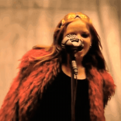 A Woman In A Red Fur Coat Singing Into A Microphone . GIF