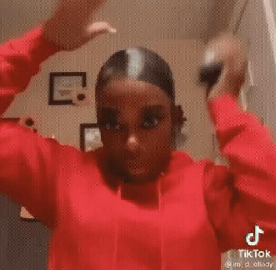 A Woman In A Red Hoodie Is Holding Her Hair Up In A Bun . GIF